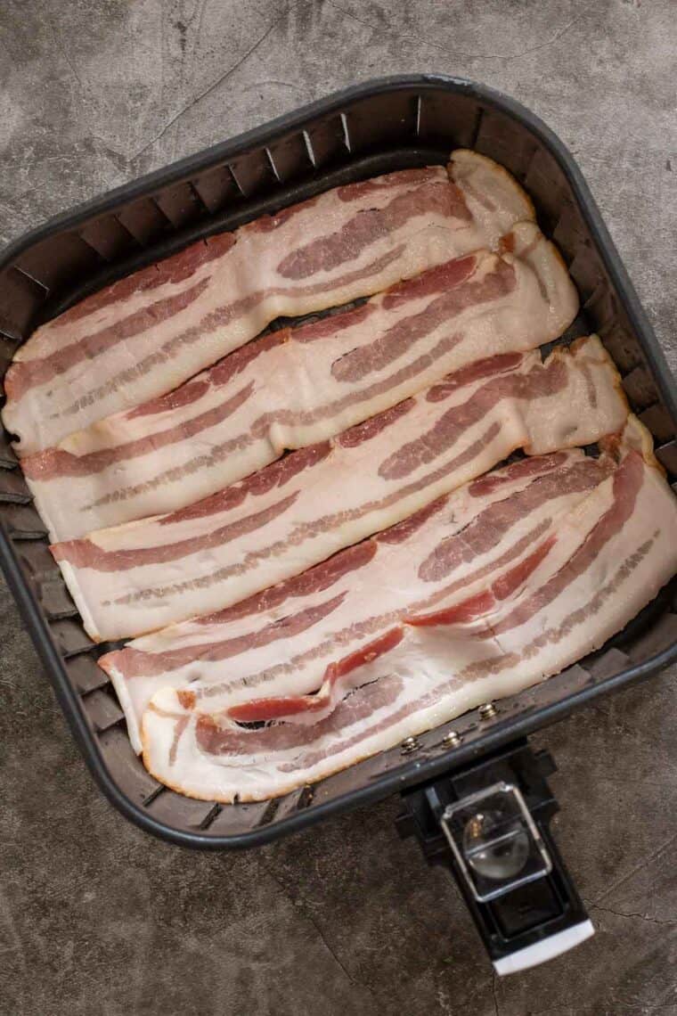 Raw bacon strips laid out in the air fryer basket. 