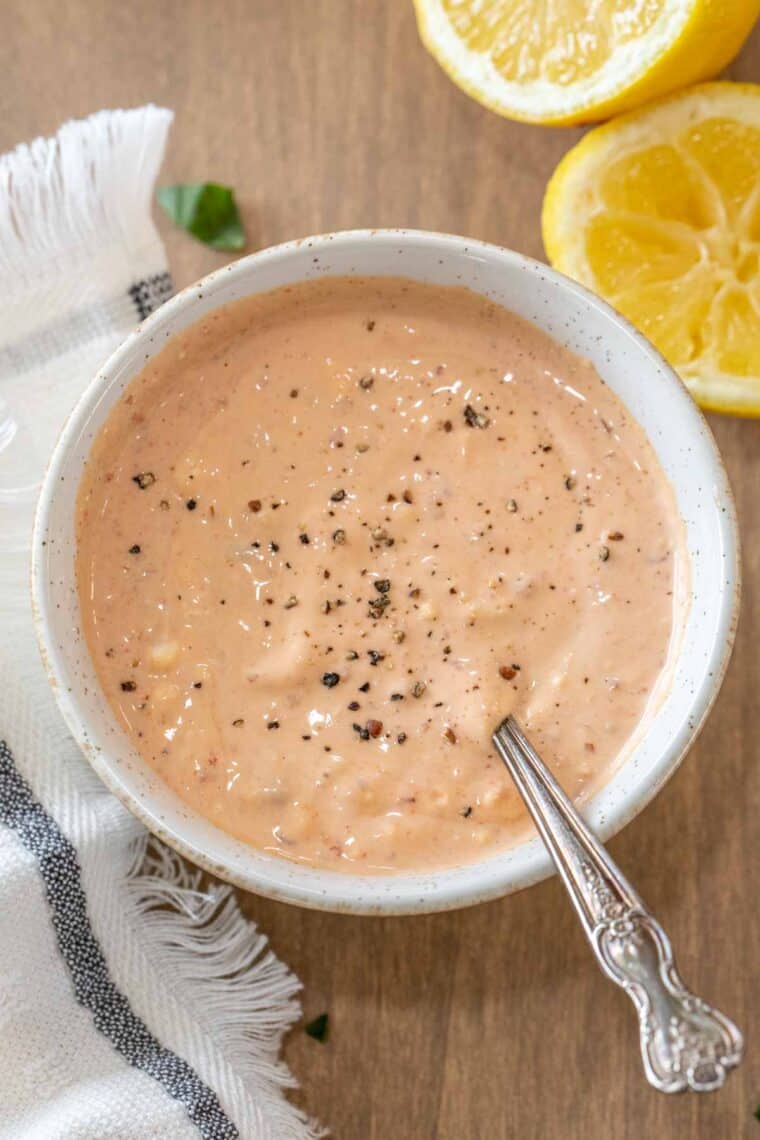 Russian dressing in a white bowl topped with black pepper with a metal spoon in it. 