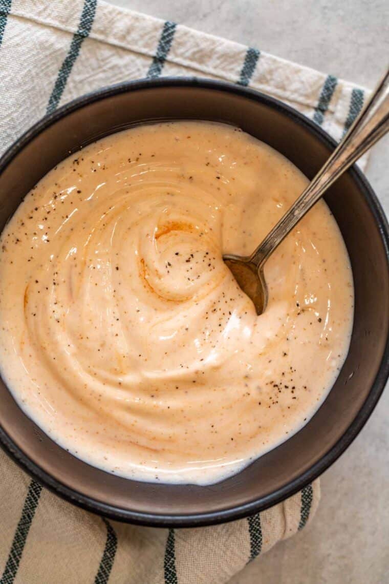 Spicy mayo in a black bowl topped with black pepper and a spoon in the bowl. 