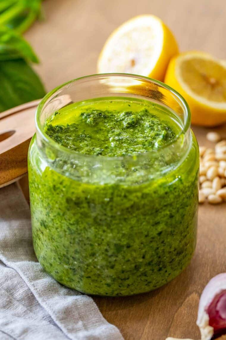 Homemade pesto sauce in a jar next to lemons and pine nuts. 