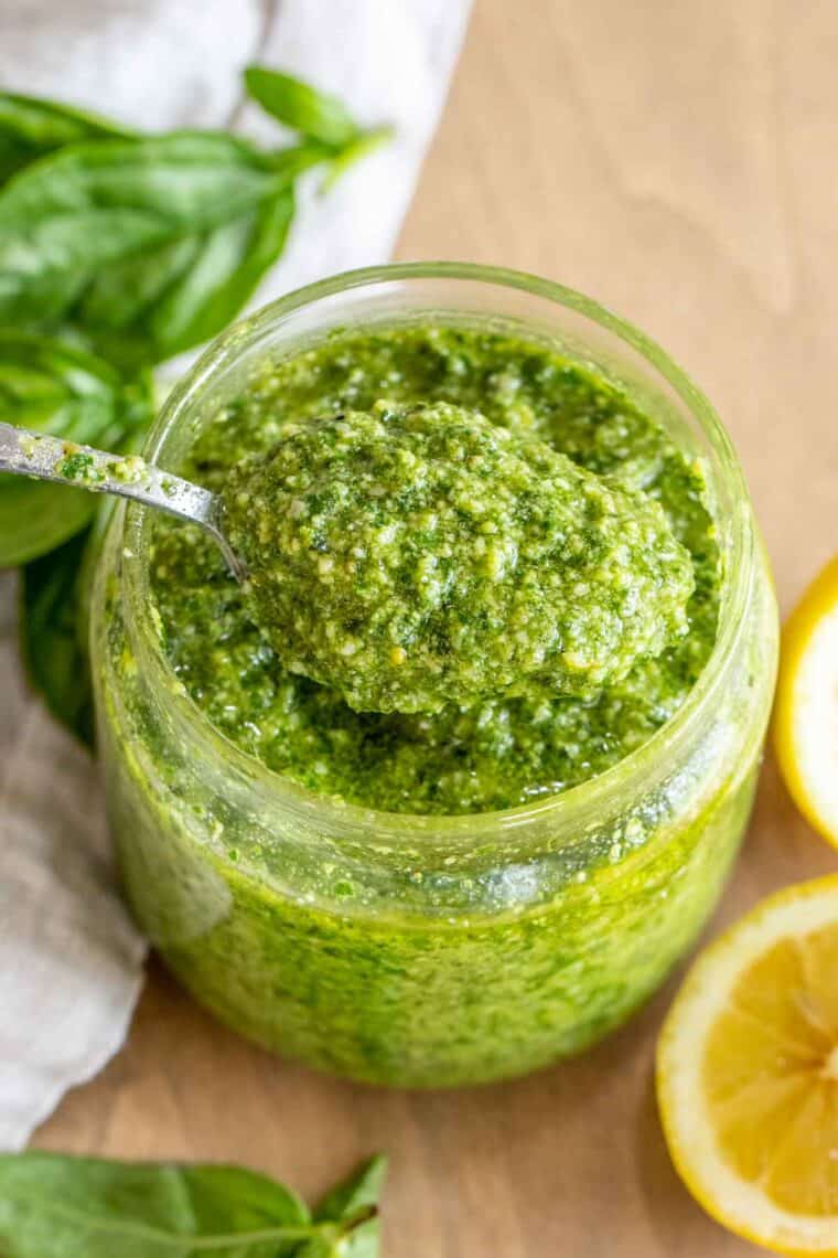 Basil pesto in a glass jar with a spoon full of pesto.
