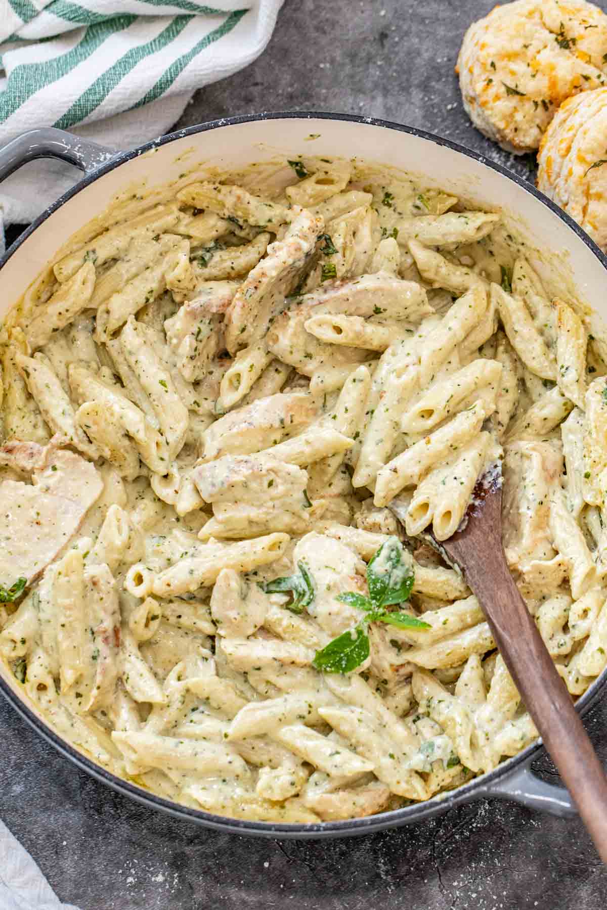 Pesto pasta in a gray deep skillet with a wooden spoon full of alfredo pasta.