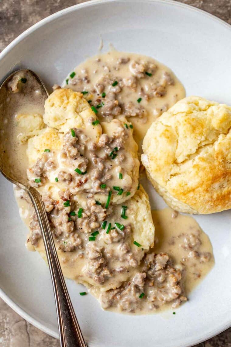 Sausage gravy over buttery flakey biscuits topped with fresh greens on a plate. 