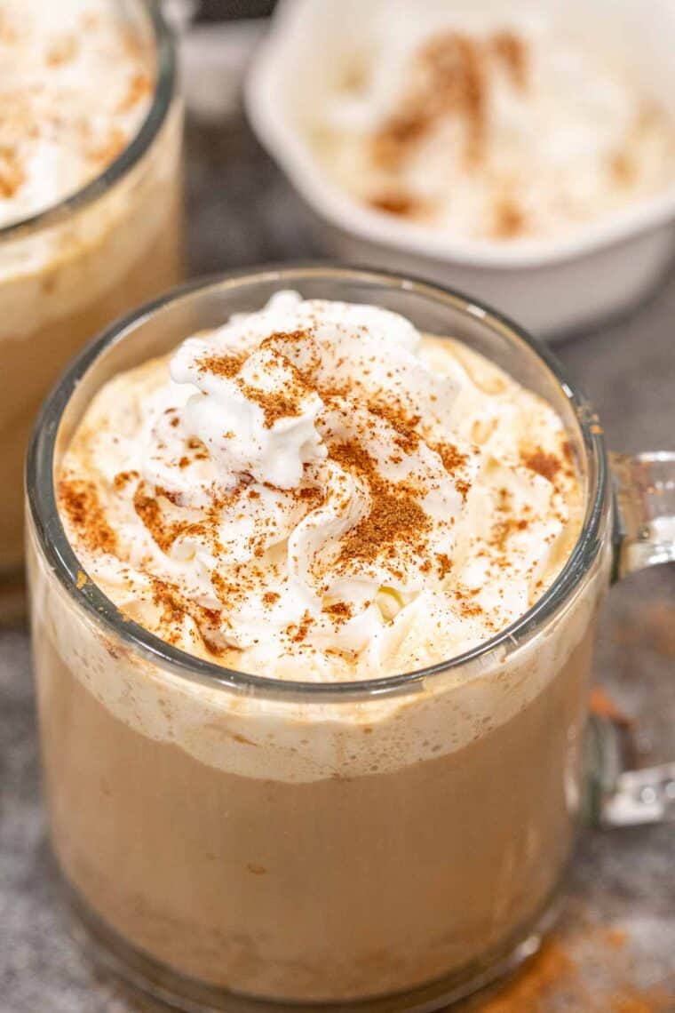 Pumpkin spice latte in a glass cup topped with whipped cream and cinnamon.