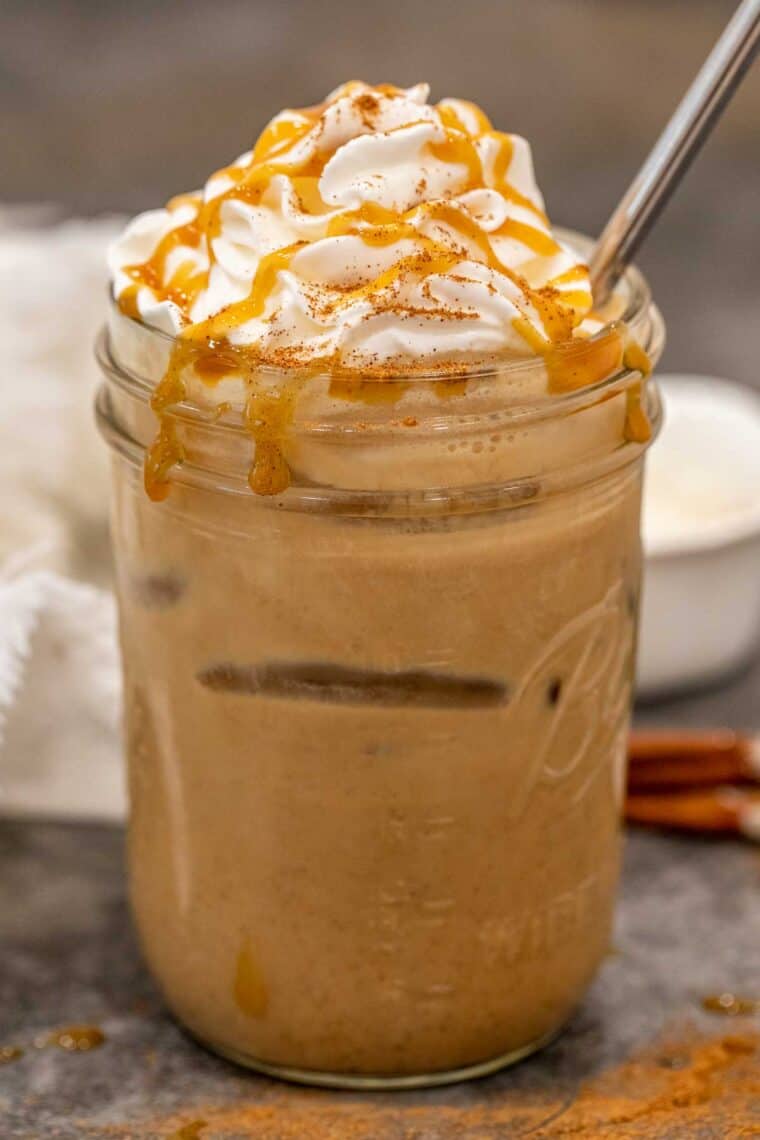 Iced pumpkin spice latte on a mason jar topped with whipped cream and syrup.