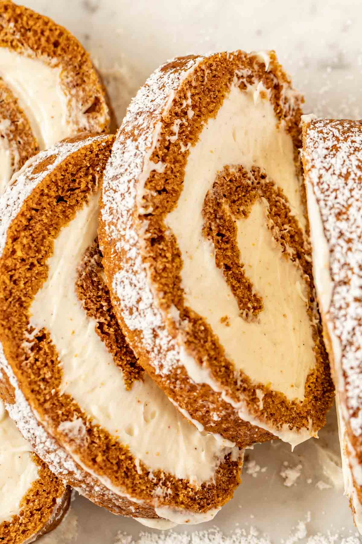 Sliced pumpkin roll laid on and stacked on top of each other topped with powdered sugar. 