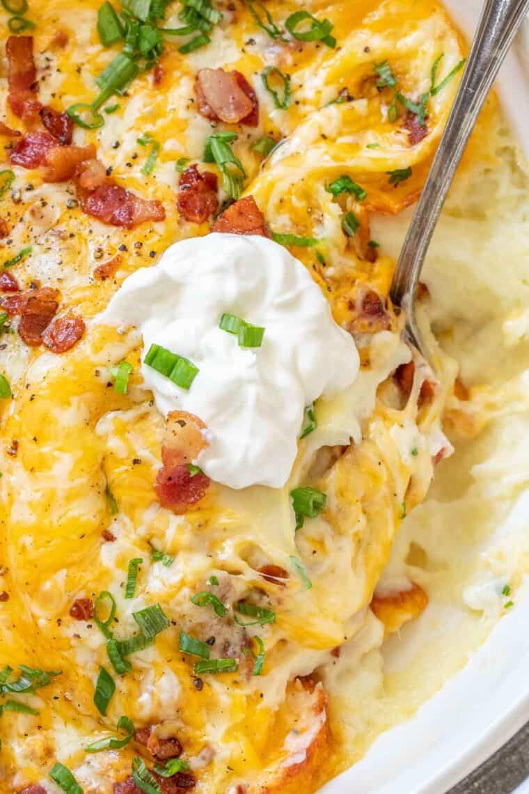 Creamy mashed potato casserole with a metal spoon and a dollop of sour cream. 