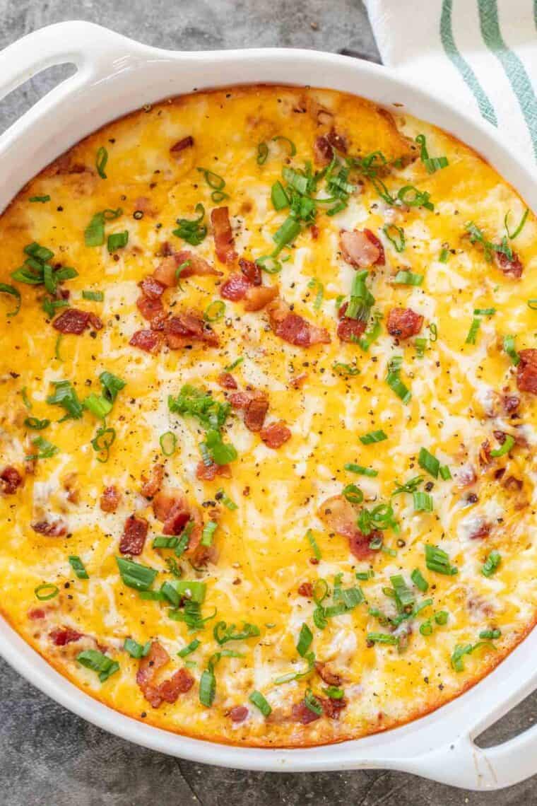 Twice baked potato casserole in a white casserole dish topped with bacon and fresh chopped green onion. 
