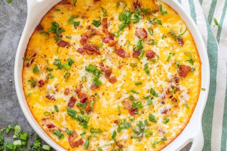 White casserole dish loaded with mashed potato casserole topped with green onion and bacon. 