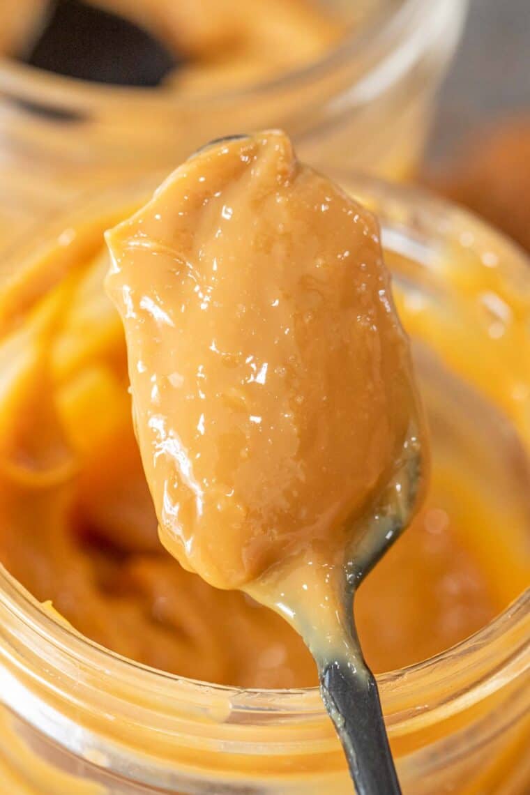 A spoonful of dulce de leche next to the  jar or dulce de leche.