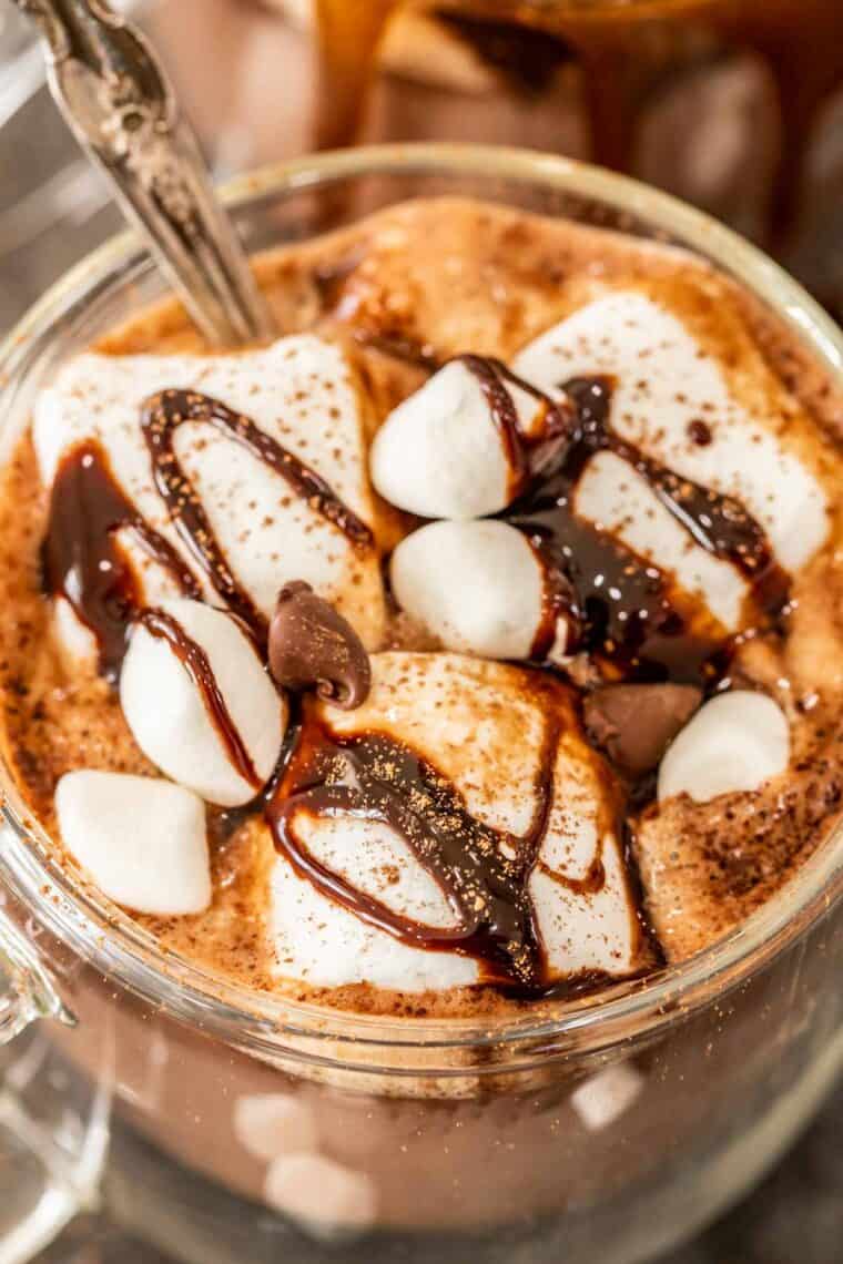 A glass mug of hot cocoa topped with marshmallows and chocolate syrup. 