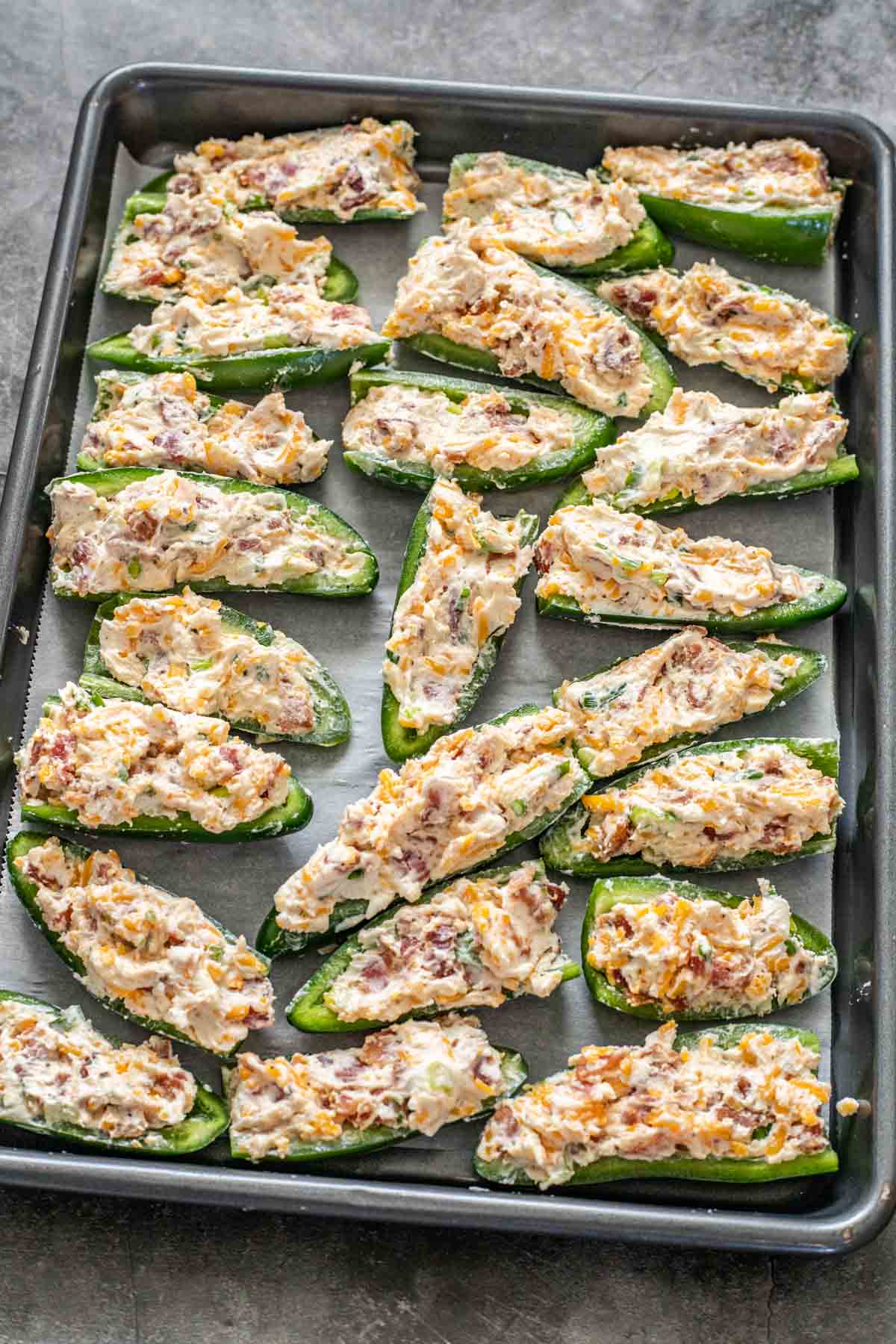 Stuffed jalapenos laid out on a baking sheet ready to be baked. 