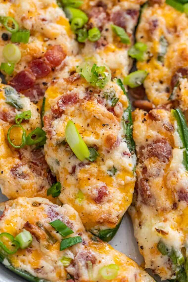 Jalapeno poppers topped with green onions and black pepper on a baking sheet. 