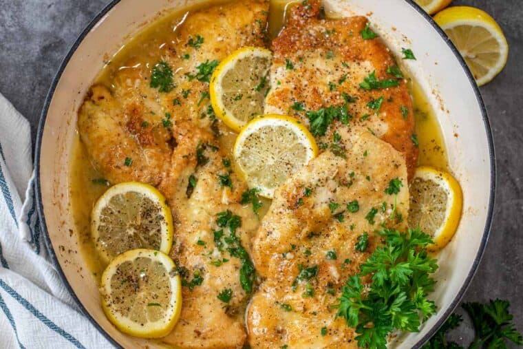Lemon chicken in a white skillet topped with fresh chopped parsley and lemon slices. 