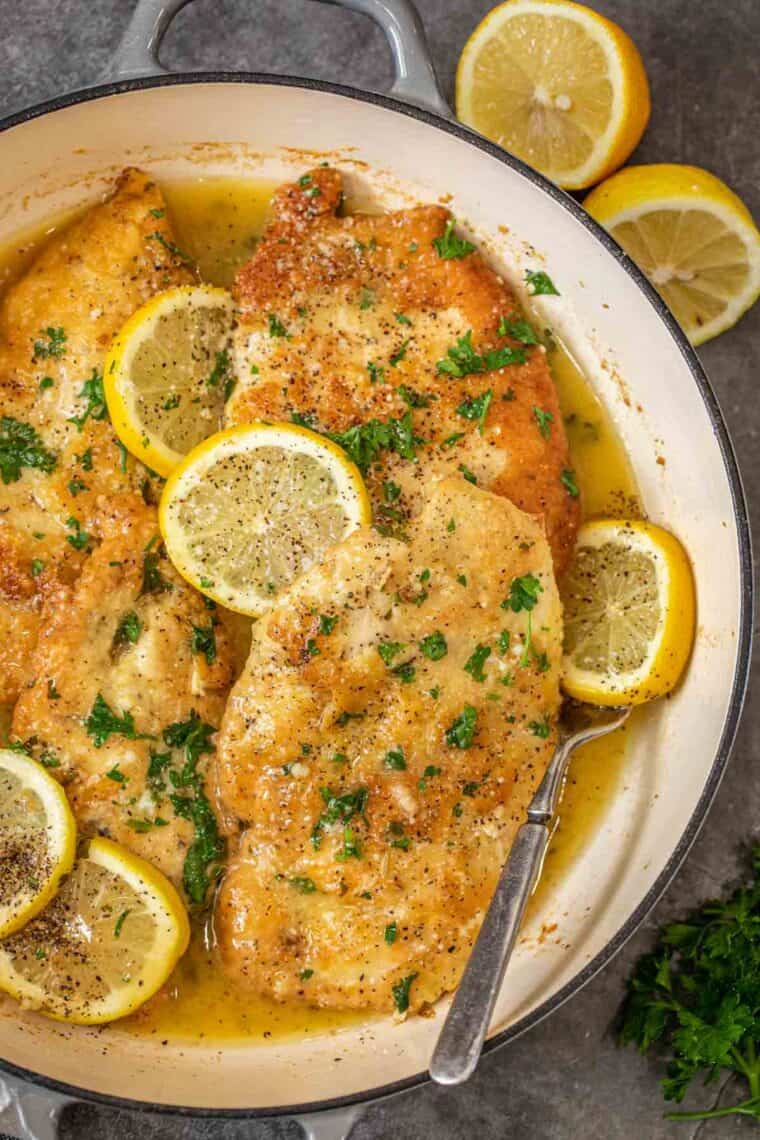 Crispy lemon chicken recipe in a skillet with a metal spoon, topped with fresh parsley.