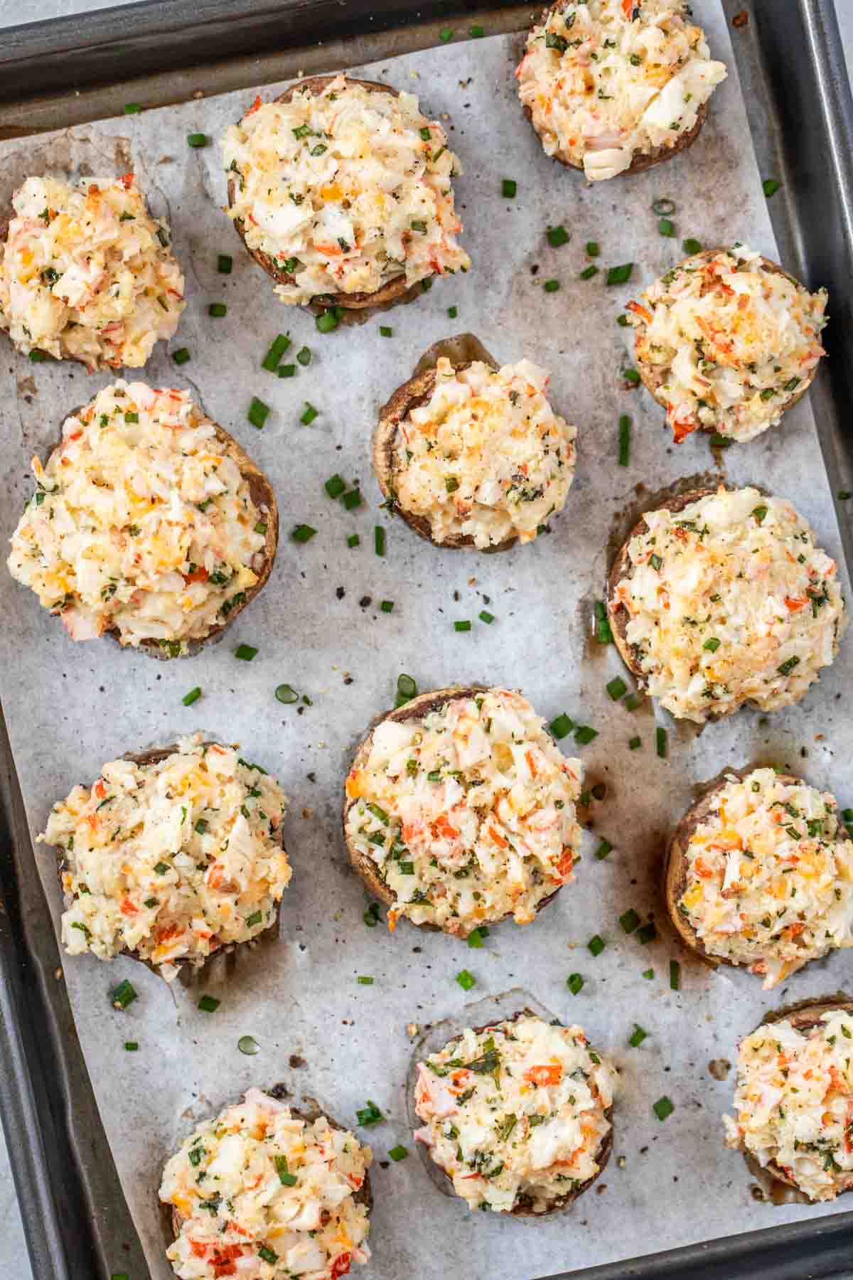 Crab stuffed mushrooms baked and laid out on a baking sheet topped with fresh chopped greens. 