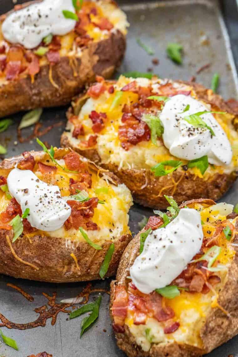 Twice baked potatoes on a baking sheet topped with green onion and sour cream. 