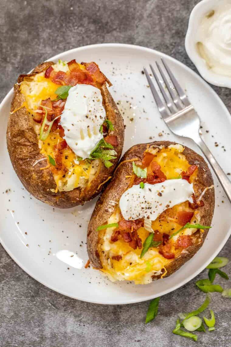 Two twice baked potatoes on a white plate with a fork topped with sour cream and green onion. 