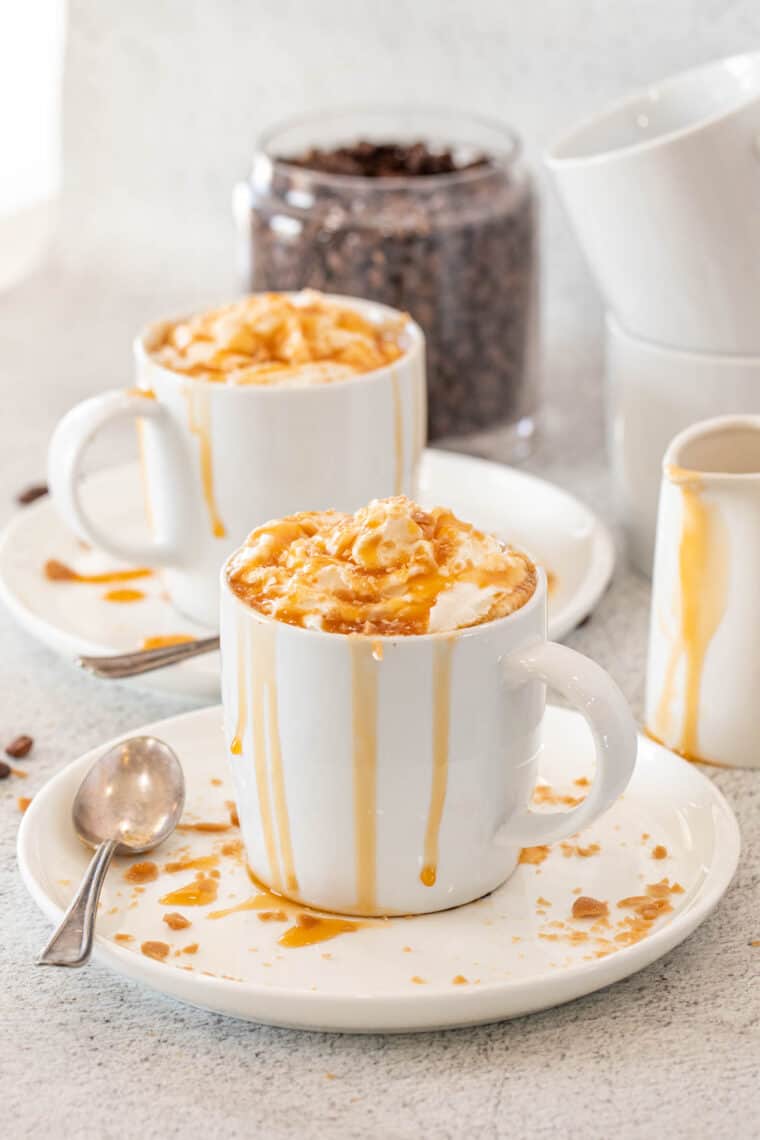 A glass mug with coffee topped with whipped cream and caramel drizzle. 