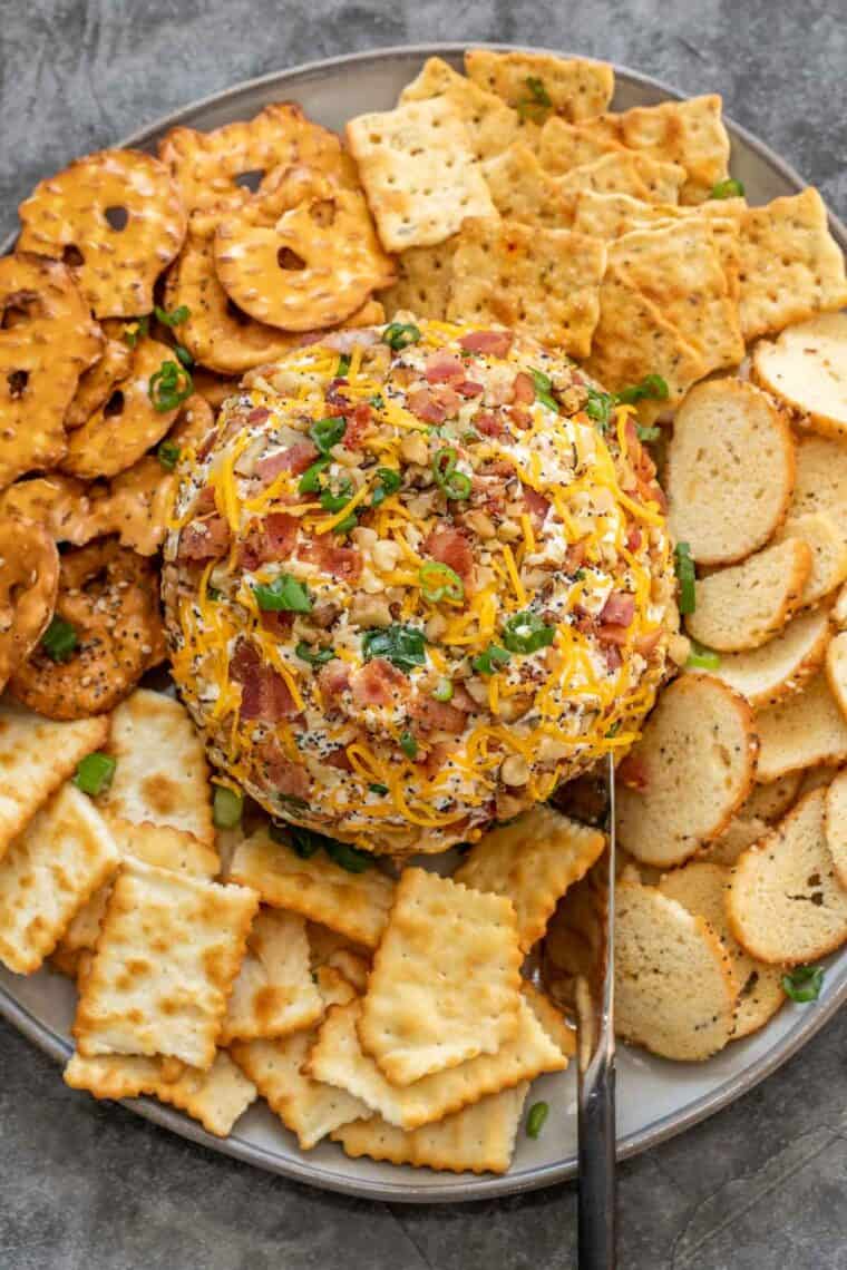 Cheese ball in a plate with different types of crackers topped with fresh chopped greens. 