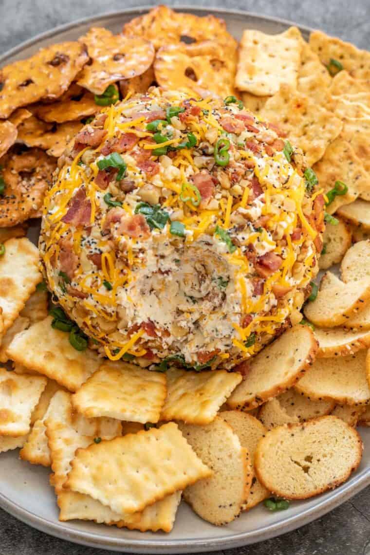 Cream cheese ball on a plate with crackers topped with fresh chopped greens. 