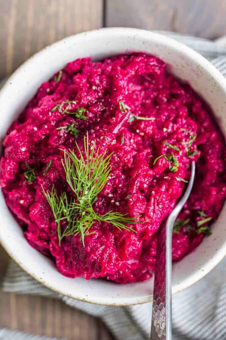 Horseradish sauce with beets in a bowl topped with fresh dill and a spoon.