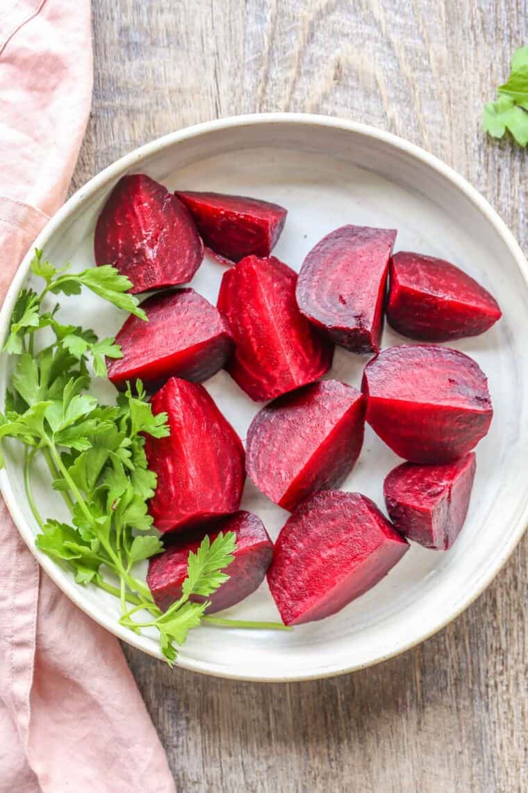 A white plate loaded with sliced cooked beets next to a pink rag. 