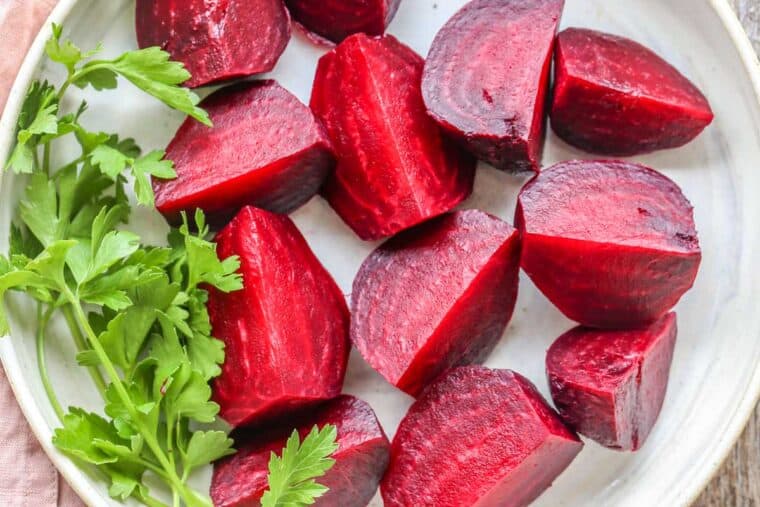 Sliced cooked beets on a white plate with a bunch of greens. 