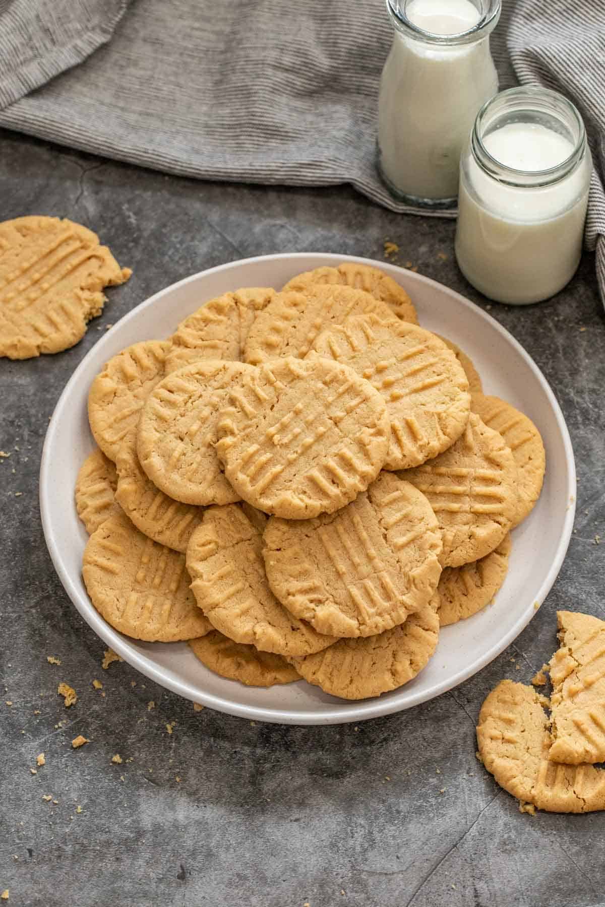 A bowl of peanut butter cookies next to two glasses of milk. 