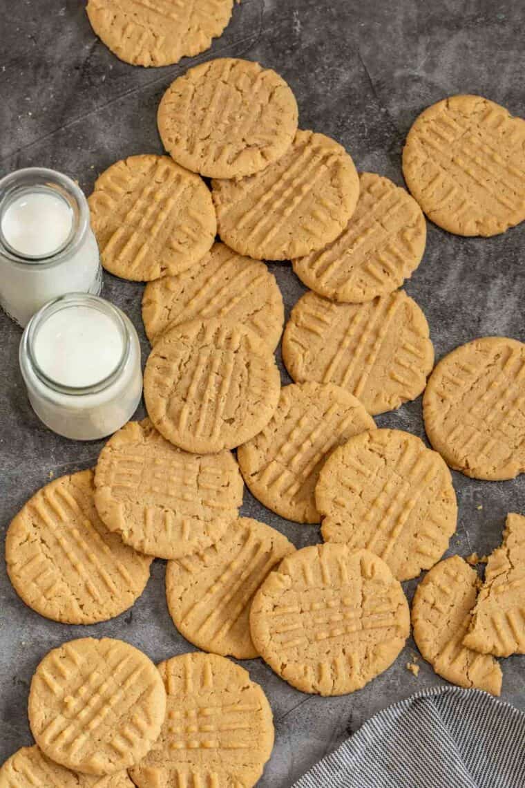 Delicious peanut butter cookies laid out next to a striped rag and cups of milk. 