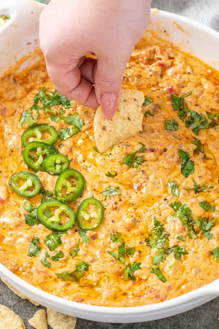 Cheesy rotel dip loaded with a white casserole dish topped with fresh greens. 