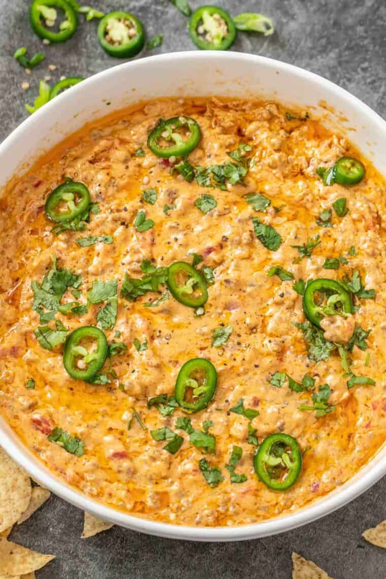 Cheesy Rotel dip in a white casserole dish topped with fresh greens and jalapeno slices. 