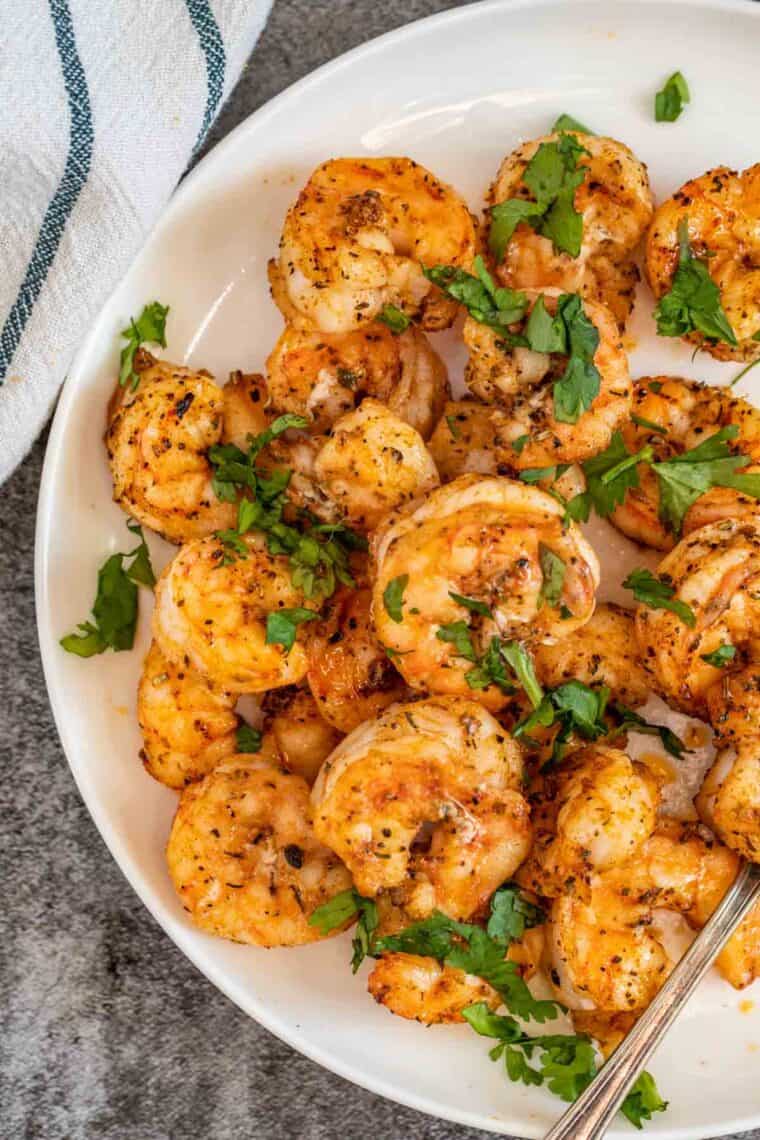 A white plate of air fryer shrimp topped with fresh chopped greens. 