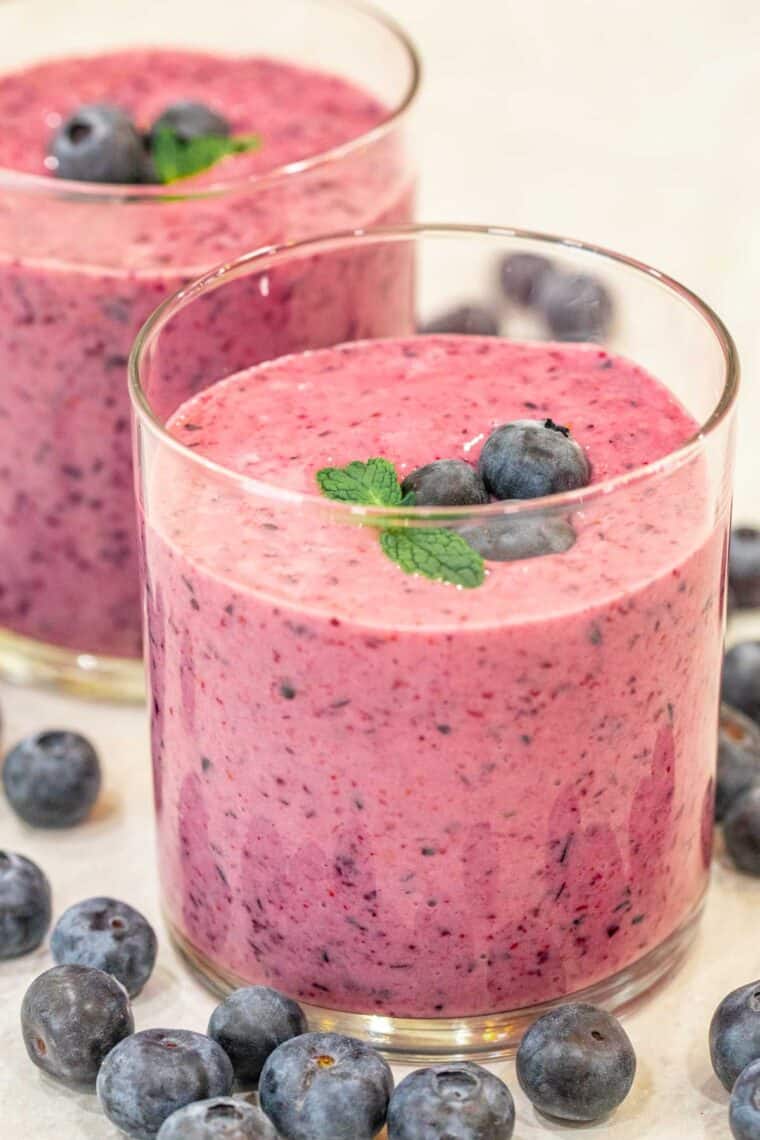 Glass cups loaded with blueberry smoothies topped with berries and mint. 