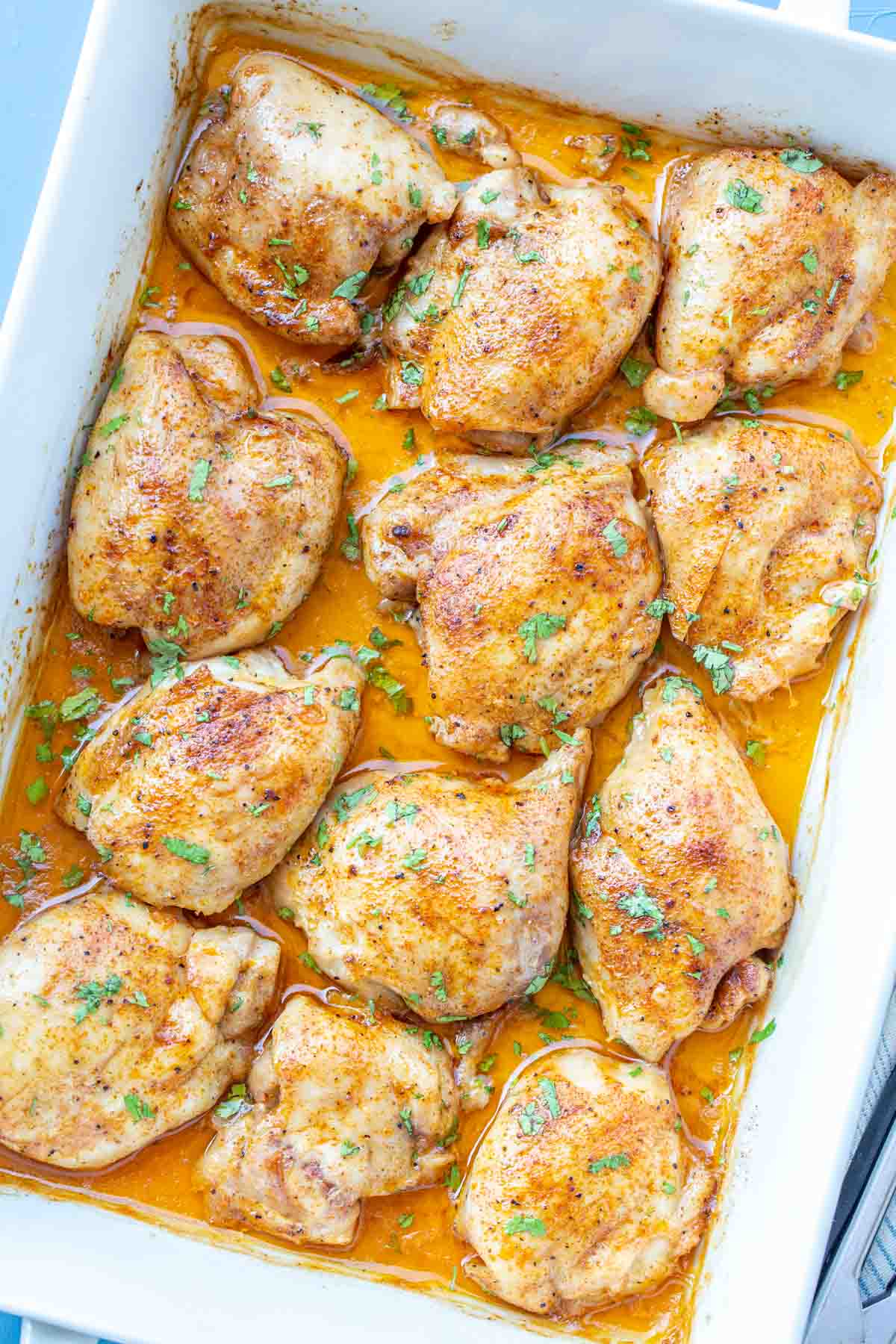 Easy baked chicken thighs in a white casserole dish topped with fresh chopped greens. 
