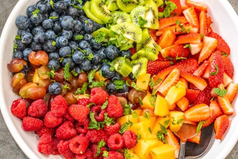 A white bowl loaded with the fresh fruit laid out topped with fresh mint. 