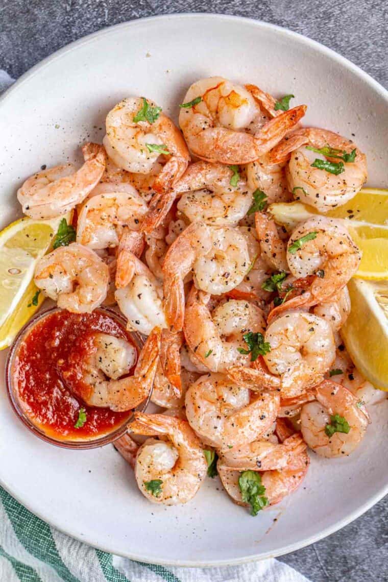 Oven baked shrimp in a white bowl topped with black pepper and chopped greens.