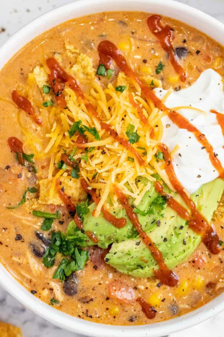 A white bowl of enchilada soup topped with shredded cheese, avocado, and sour cream. 