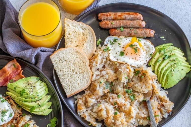 Plates loaded with shredded potatoes with eggs, sausage links, and toast. 
