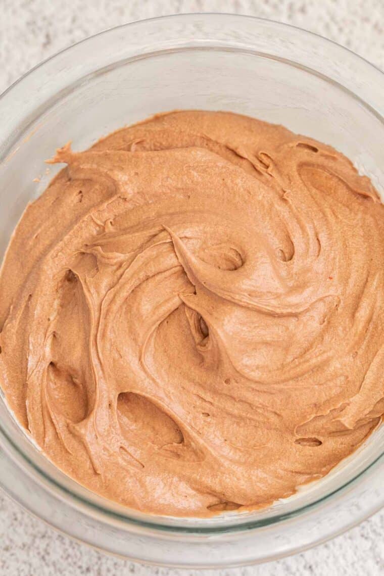 A glass bowl full of chocolate buttercream frosting. 