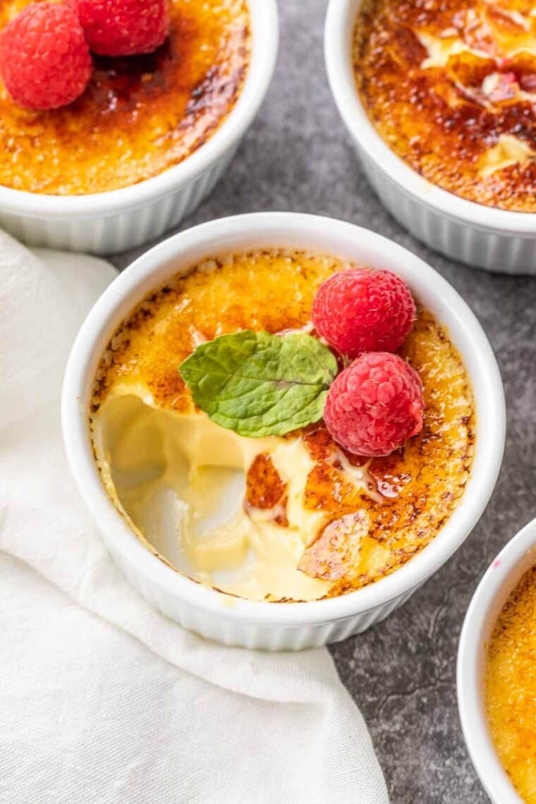 Classic creme brulee into white ramekins topped with raspberries and mint. 