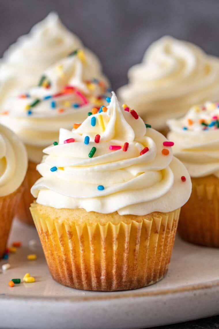 Classic vanilla cupcakes topped with vanilla buttercream and sprinkles on a plate. 