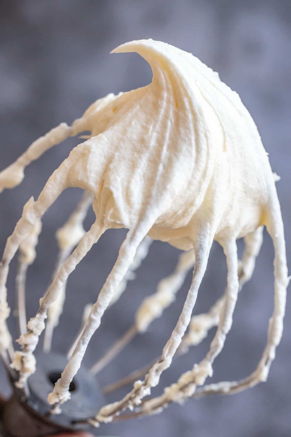 A whisk with cream cheese frosting on it. 