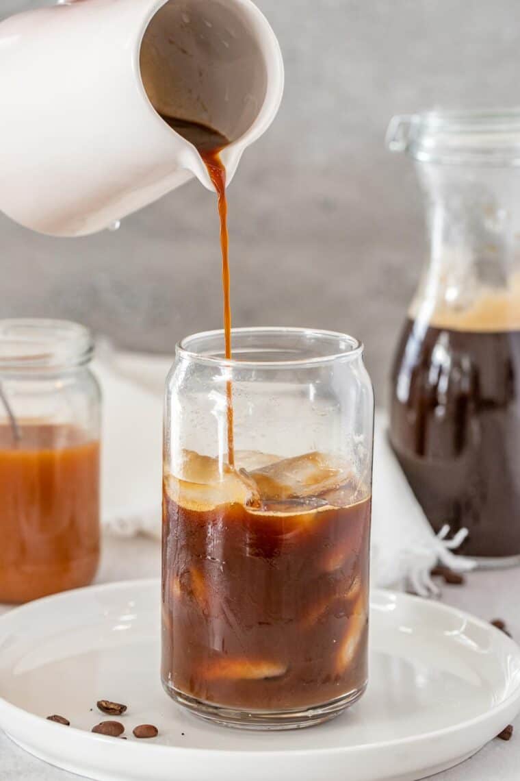 Strong coffee being poured into a glass cup over ice.