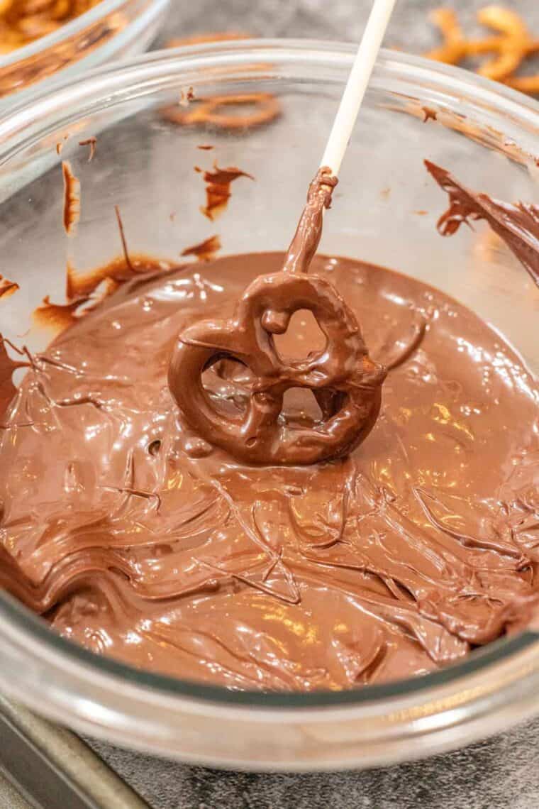 A pretzel being dipped into the melted chocolate. 