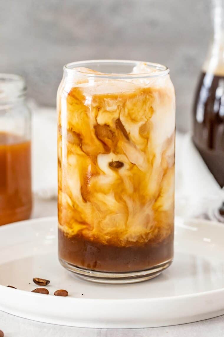 A glass of iced caramel latte on a white plate.