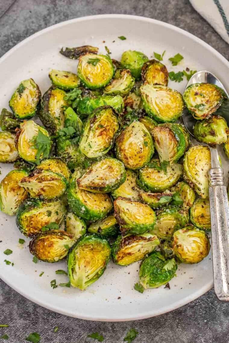 Brussel sprouts in a white plate topped with fresh greens. 