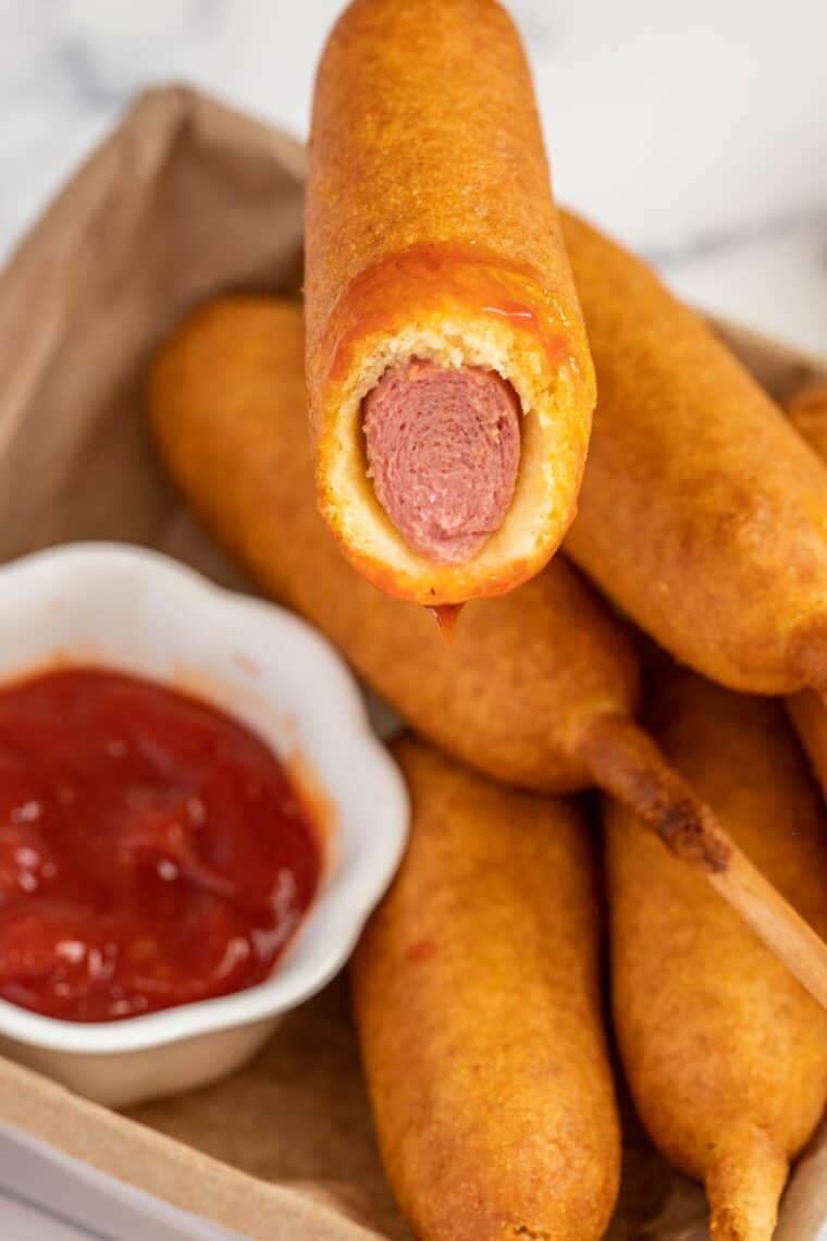 Corn dogs in a basket with one being bitten into. 