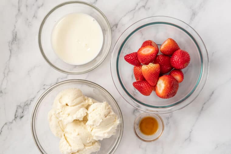 Ice cream, milk, strawberries, and vanilla all in bowls. 