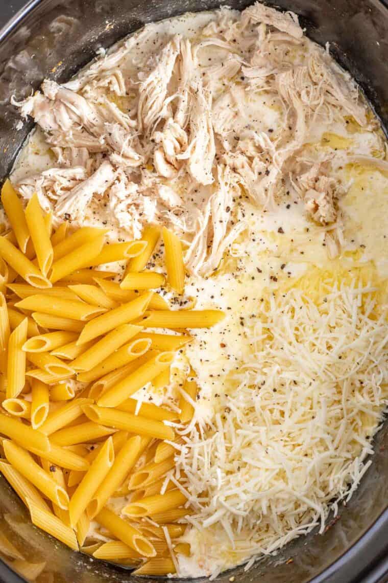 Shredded chicken, penne pasta, and shredded cheese on the slow cooker. 